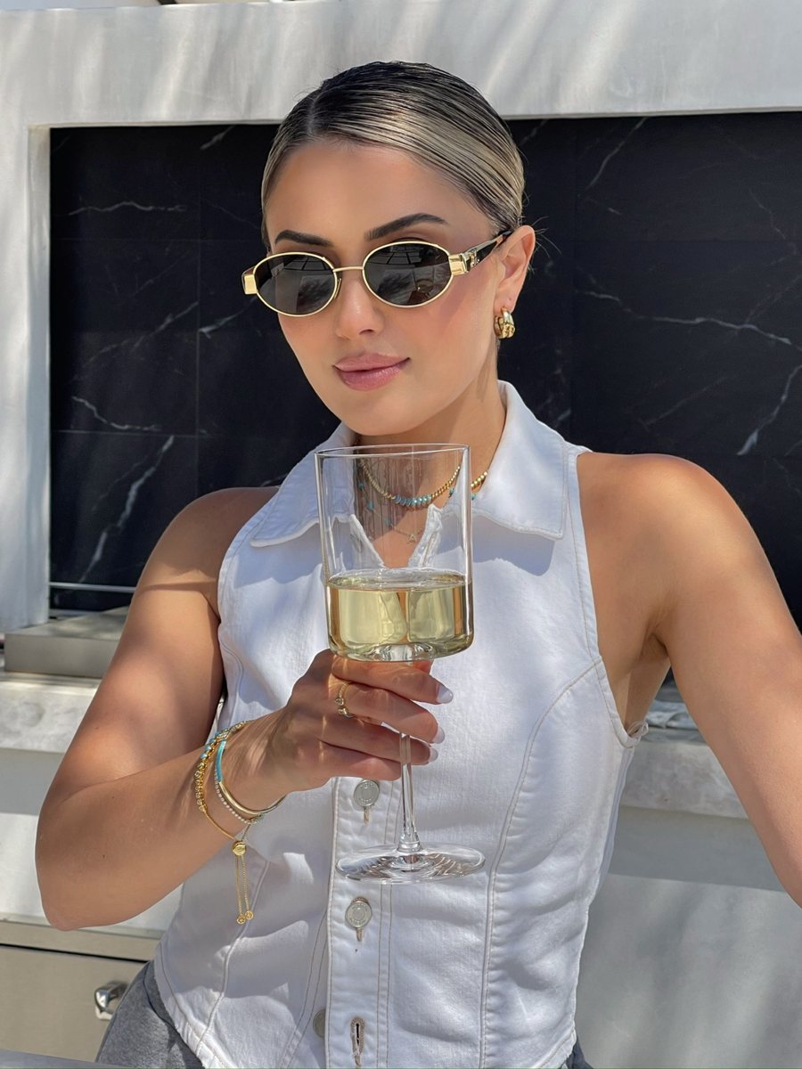 Woman in gold sunglasses holding a glass of white wine