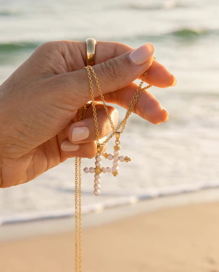 AI video: hand holding pearl cross necklaces at the beach